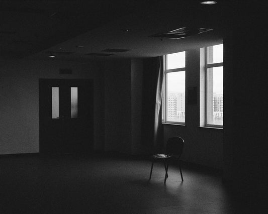 An empty chair beside a window in a quiet, bare room — black-and-white film photograph